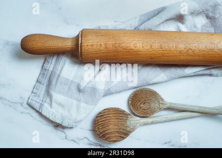 Vista dall'alto di cucchiai in legno, perno rotante e tovagliolo da tè su un piano di lavoro in marmo della cucina Foto Stock