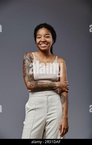 Ritratto verticale di sicura donna nera con tatuaggi che guardano la fotocamera e sorridono Foto Stock