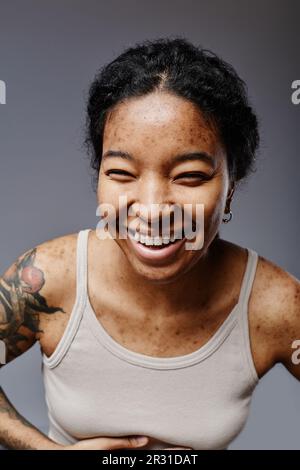 Ritratto verticale di giovane donna nera guardando la macchina fotografica e ridendo con comica emozione Foto Stock