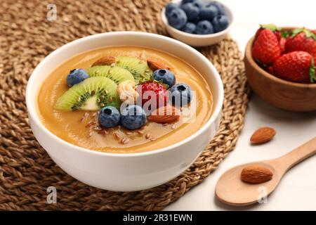 Deliziosa ciotola per frullati con frutti di bosco freschi, kiwi e noci sul tavolo, primo piano Foto Stock