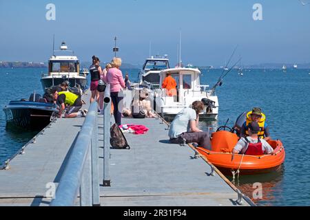 Gente vacanzieri, barche, bambini che godono il sole sul molo in primavera a Dale Pembrokeshire West Wales Regno Unito Gran Bretagna Maggio 2023 KATHY DEWITT Foto Stock