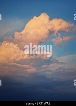 Nuvole di tempesta di cumuli illuminate dal sole, luce del tramonto rosa e dorata. Cielo da sogno, sfondo celeste verticale Foto Stock