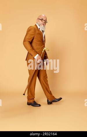 Ritratto di uomo serio, bearded, maturo, calvo in abito elegante e classico e bastone da passeggio che si posa sullo sfondo dello studio Foto Stock