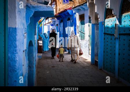 Persone che camminano per le strade tra le ombre e il sole tracciando le forme sulle pareti delle case a Chefchaouen una città nel nord-ovest del Marocco, fo Foto Stock