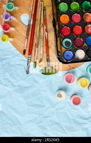Posa piatta di pitture colorate, pittura tavolozza e pennelli su sfondo blu, arte, pittura e hobby concetto, vista dall'alto, copia spazio. Foto Stock