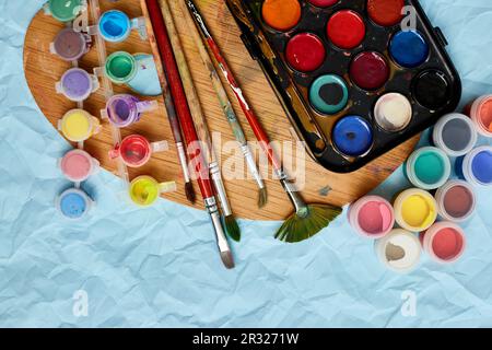 Posa piatta di pitture colorate, pittura tavolozza e pennelli su sfondo blu, arte, pittura e hobby concetto, vista dall'alto, copia spazio. Foto Stock