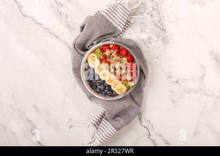 Ciotola di granola di avena con yogurt, lamponi freschi, mirtilli, fragole, banana e noci su sfondo bianco per una sana colazione. Vista dall'alto. Foto Stock