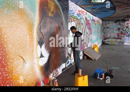 Londra, Inghilterra - 26 maggio 2013: Un giovane artista di graffiti spray sta dipingendo su una parete di cemento la testa di un leone; questo graffiti e altri sono sulla R Foto Stock