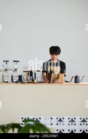 Giovane uomo penoso che lavora nel coffee shop, che usa il filtro contagocce phin per preparare il caffè Foto Stock