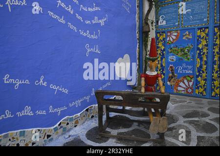 Pinocchio su una panca in legno e murale dipinto a mano con coloratissima iconografia popolare siciliana a Borgo dei Parrini Sicilia. Foto Stock