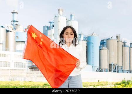 Preoccupata ragazza asiatica con bandiera della cina che si trova di fronte allo scenario industriale Foto Stock