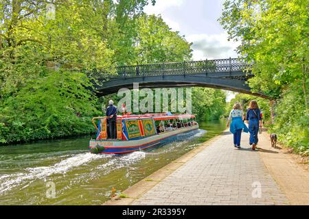 London Regents Canal Springtime la barca Jenny Wren che passa sotto il ponte e gli escursionisti cani sul sentiero Foto Stock