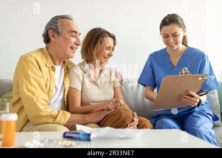 Visita al paziente. Infermiera che parla con la coppia anziana, tenendo appunti in conversazione con l'uomo e la donna anziani Foto Stock