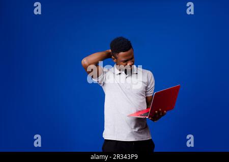 Ritratto di un uomo d'affari africano stressato che porta con sé un computer portatile con la mano sulla testa isolato su sfondo blu Foto Stock