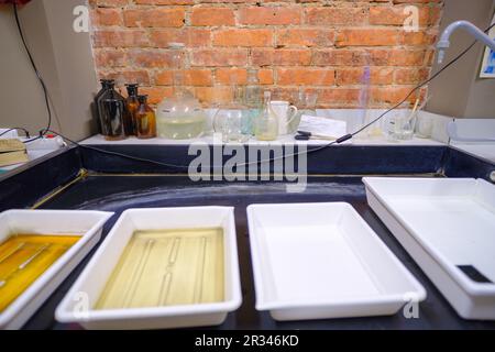 Serbatoio di sviluppo con chimica. Rotoli di pellicola fotografica, cassetta, timer e flaconi di reagenti chimici sullo sfondo. Foto Stock