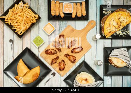 Set di fast food, con un vassoio di patatine, cachapa venezuelana, empanadas, arepas, ali di pollo barbecue e salse Foto Stock