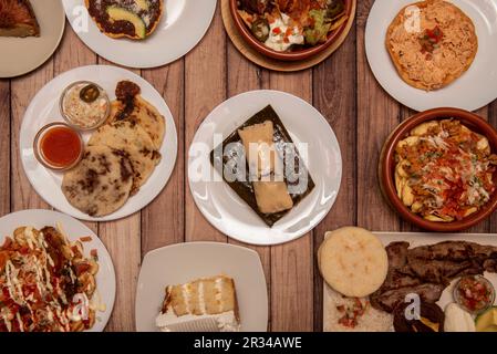 Set di piatti latinoamericani e fusion con tamales, patate con salse, arepas assortite, roast beef e crostate Foto Stock