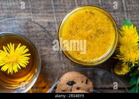 Marmellata dolce di petali gialli maturi di fiori di dente di leone, arancia, limone e zucchero sul tavolo di legno con tè e biscotti, vista dall'alto, primo piano Foto Stock