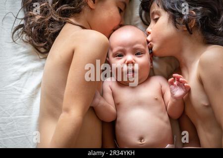 due sorelle più anziane con capelli scuri che baciano la sorella neonato spaventato Foto Stock