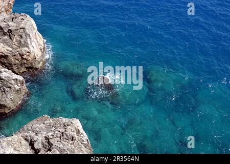 Vista dall'alto litorale roccioso all'acqua di mare trasparente e azzurra con schiuma nelle giornate di sole Foto Stock