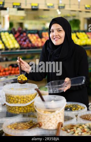 Giovane donna in hijab raccolta olive in supermercato Foto Stock