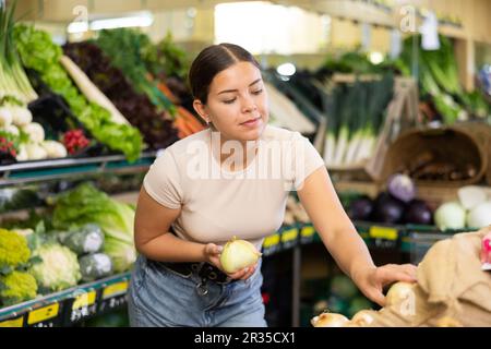 Giovane donna acquirente sceglie cipolle nel supermercato Foto Stock