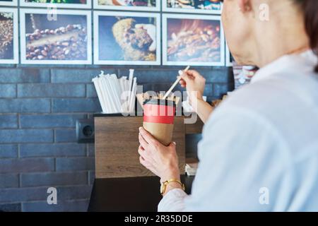 Alicante, Spagna, 12.05.2023, Donna con takeaway tazza di carta vicino al banco self-service in caffetteria Foto Stock
