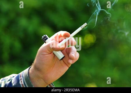 Acceso sulla sigaretta e un accendisigari in una mano di un fumatore Foto Stock