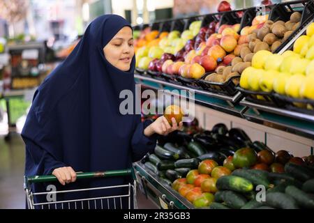 Giovane donna in hijab compra pomodori al negozio di alimentari Foto Stock