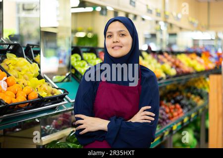 Ritratto di amichevole venditore femminile in hijab e grembiule nella sezione della drogheria del supermercato Foto Stock