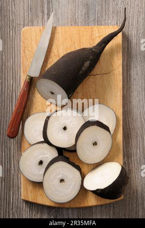Rafano nero, parzialmente affettato, su un tagliere Foto Stock