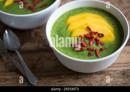 Un frullato di verde in una ciotola con le fette di mango e bacche di goji Foto Stock