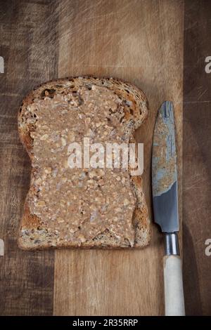 Pane tostato integrale con burro di arachidi spalmato su un tagliere con un coltello Foto Stock