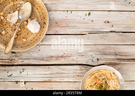 Hummus in una ciotola e su un piatto con un cucchiaio, aglio e ceci Foto Stock