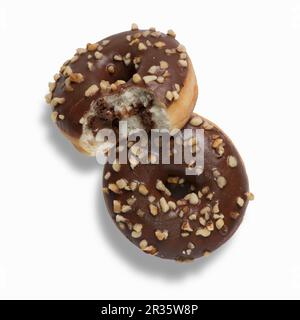 Due nutella ciambelle con la glassa al cioccolato e nocciole tritate, uno con un morso prelevato Foto Stock