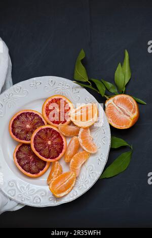 Fette di arance sanguigne e mandarin segmenti su una piastra bianca Foto Stock