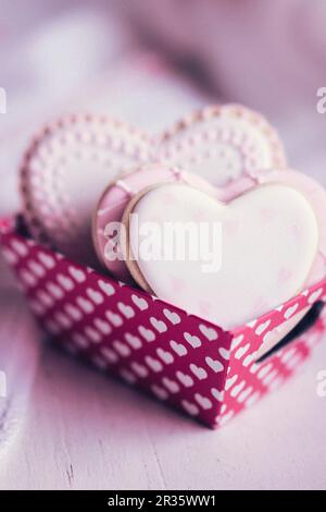 Biscotti color pastello a forma di cuore in una scatola di carta decorata con cuori Foto Stock