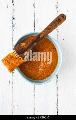 Salsa Harissa in una ciotola blu con un pennello Foto Stock