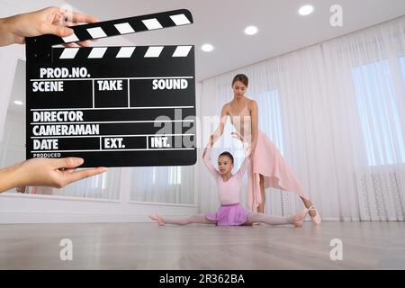 Ripresa di un filmato. Seconda macchina fotografica assistente che tiene il clapperboard davanti all'insegnante di balletto e alla ragazza (attori) presso lo studio di danza (set cinematografico) Foto Stock