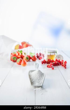 Una paletta di zucchero su una superficie di legno bianco con disposizione di frutta con fragole, lingonberle e mele sullo sfondo Foto Stock