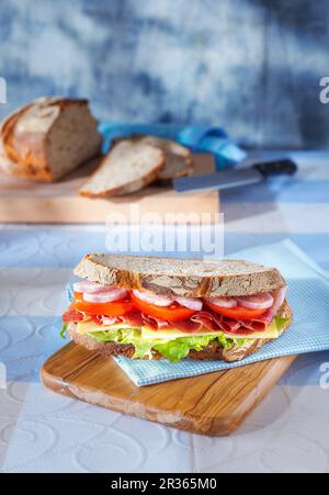 Un panino su un tovagliolo azzurro su un asse di legno con un pane affettato sullo sfondo Foto Stock