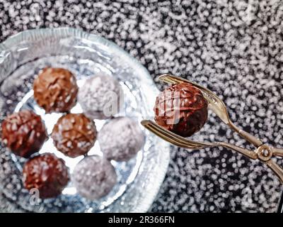 Pinze praline che tengono una pralina al tartufo su una lastra di vetro di vari tartufi Foto Stock