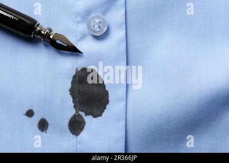 Macchie di inchiostro nero su camicia e penna blu chiaro, vista dall'alto. Spazio per il testo Foto Stock