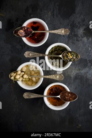 Vari tipi di tè su cucchiai d'annata sopra le ciotole (visto dall'alto) Foto Stock