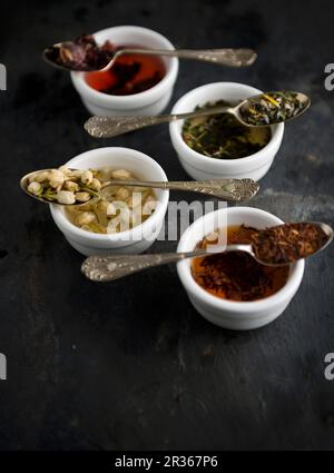 Vari tipi di tè su cucchiai d'annata su ciotole Foto Stock