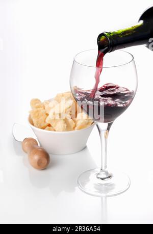 Il vino rosso è versata in un bicchiere con una ciotola di parmigiano in background Foto Stock