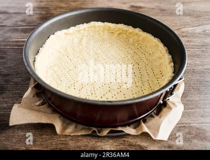 La pasta frolla in un colore rosso scuro springform tin con la carta da forno su una tavola di legno Foto Stock