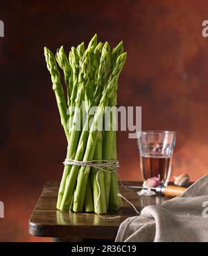 Un fascio di asparagi verdi su una tavola di legno con vino e aglio Foto Stock