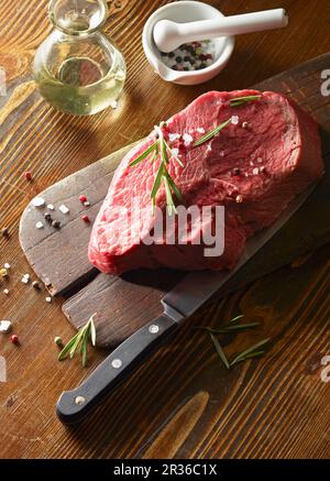 Materie di filetto di manzo (450 g) su una tavola di legno con rosmarino e pepe colorati Foto Stock