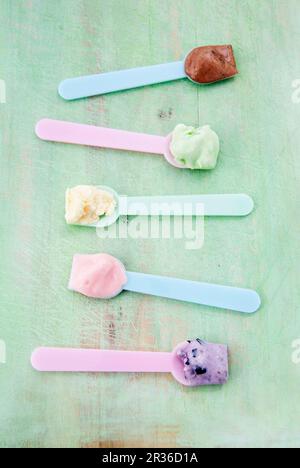 Vari tipi di gelato su cucchiai di gelato: Vaniglia, fragola, cioccolato, mirtillo e menta Foto Stock